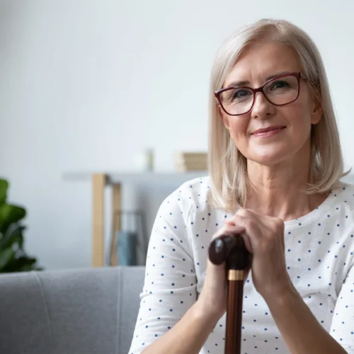 A woman looks at the camera with a smile on her face with her hands resting centrally on her walking stick