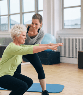 woman squatting with arms out and support from exercise physiologist