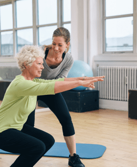 woman squatting with arms out and support from exercise physiologist