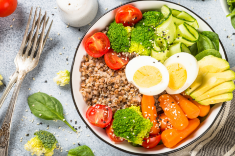 Bowl, set out on a table with cutlery, containing eggs, grains, salad, vegetables