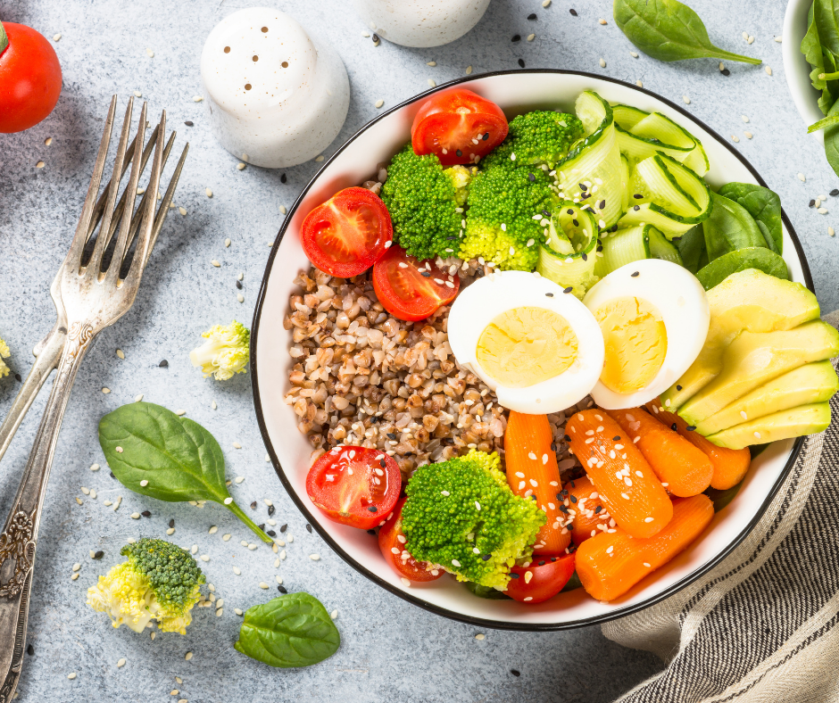 Bowl, set out on a table with cutlery, containing eggs, grains, salad, vegetables