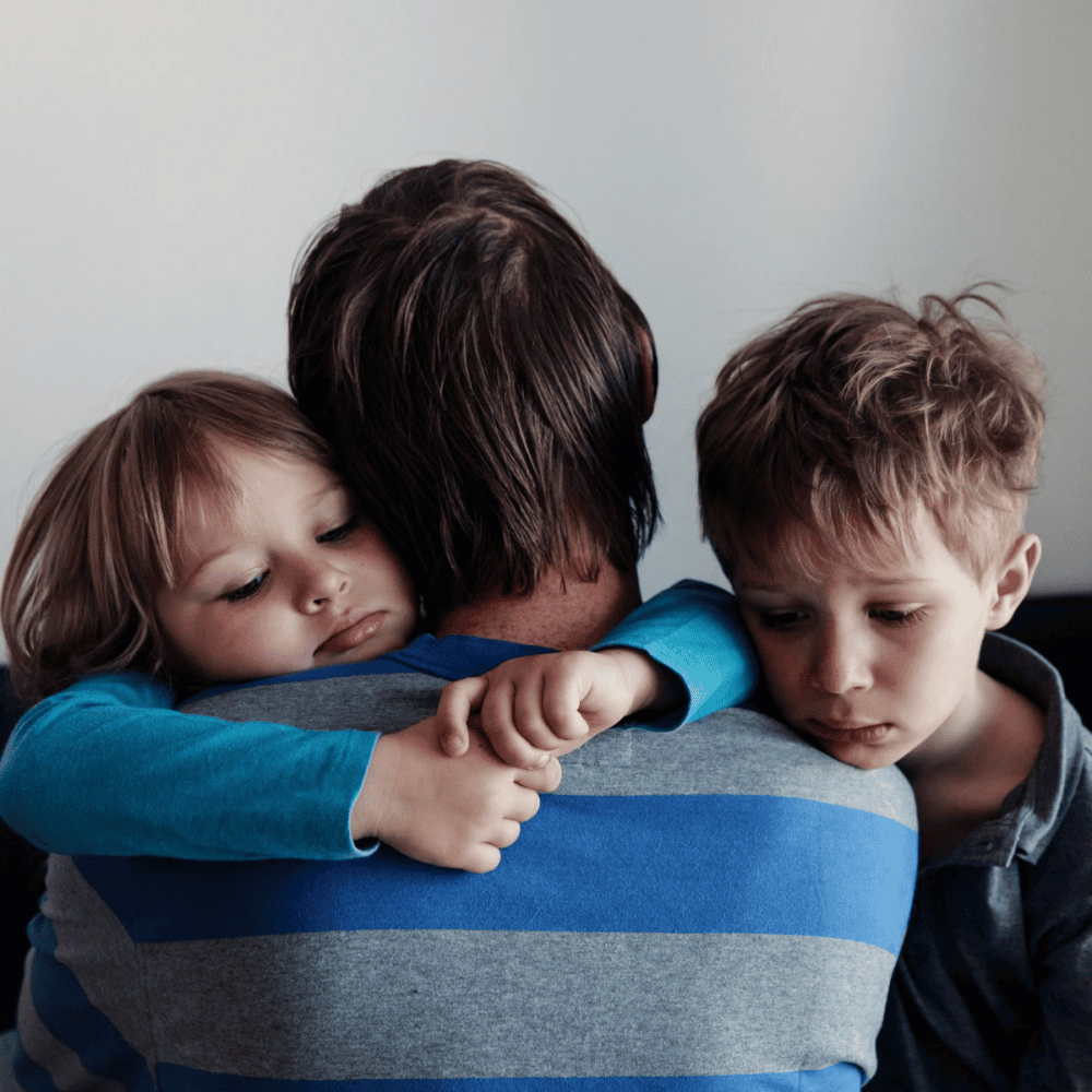 Two young boys hugging their dad